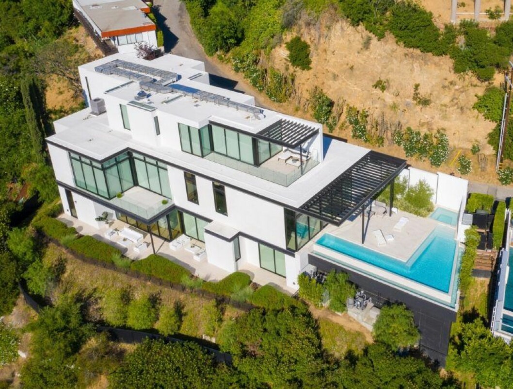 Här är det gigantiska huset som Ariana Grande har köpt. ett stort hus i vitt och glas med en pool utanför.