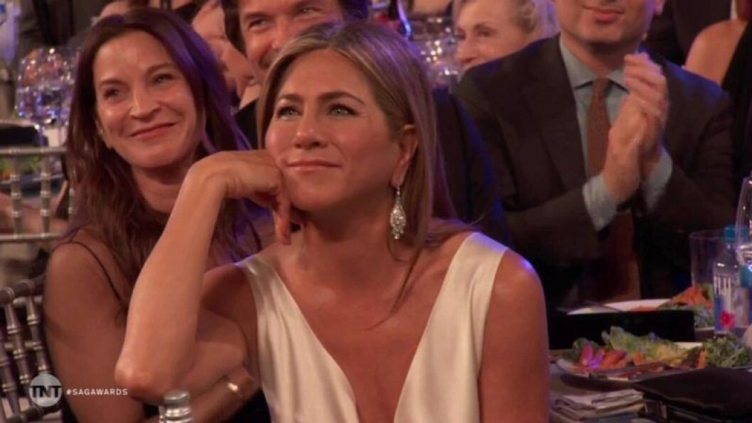 Jennifer Aniston lutar huvudet i sin ena hand och ler