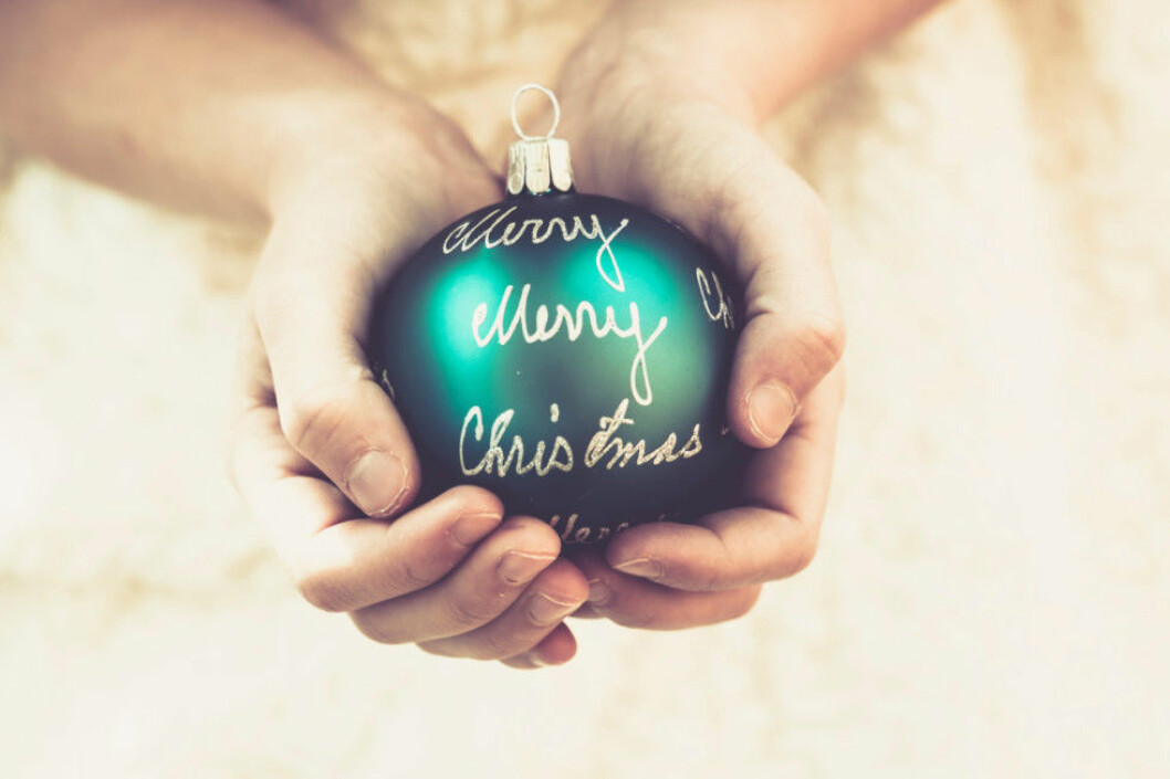 Girl's hands holding green Christmas bauble with the words 'Merry Christmas'