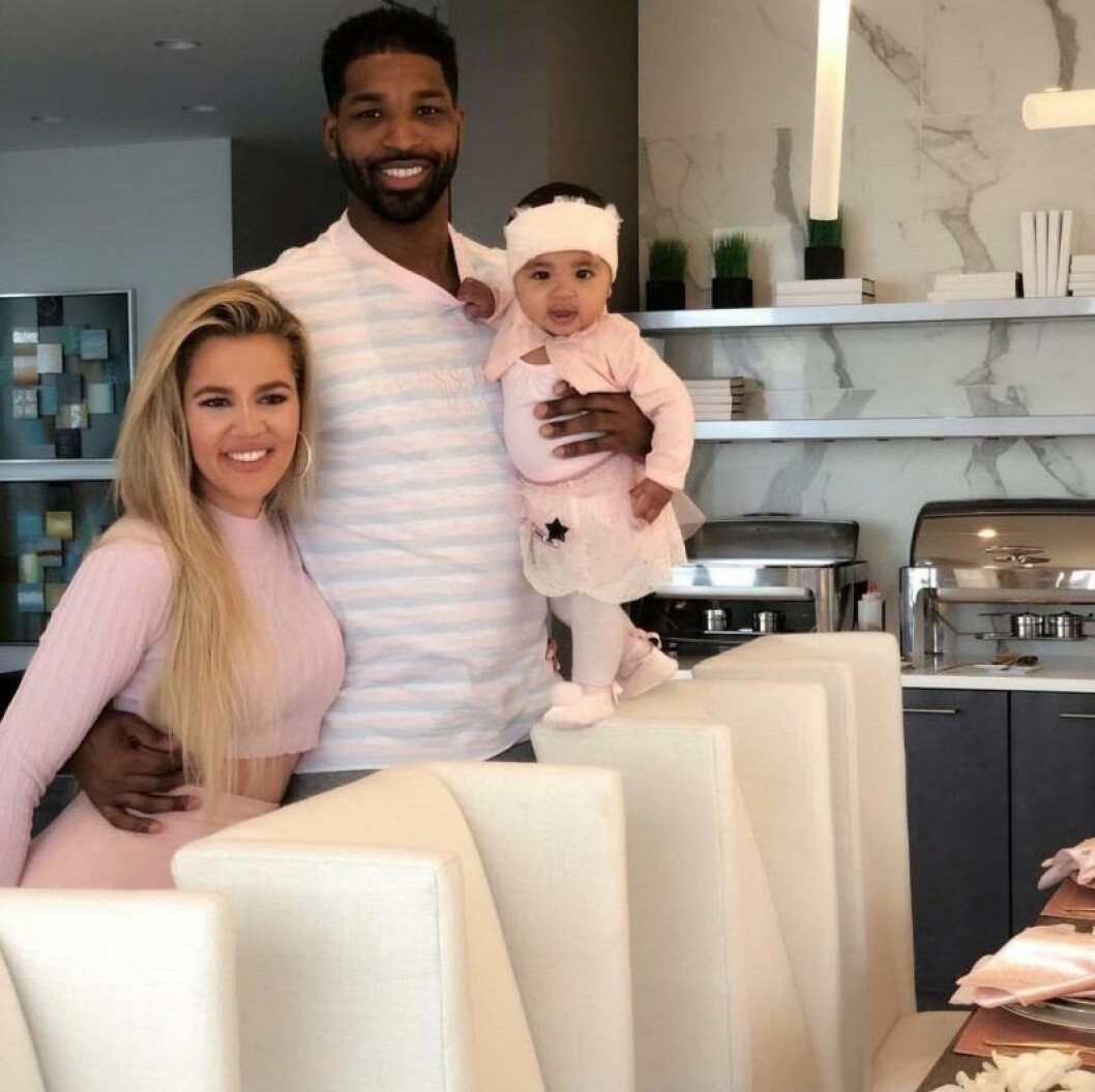 Bara veckor efter att denna bilden togs gjorde paret slut. Khloé Kardashian och Tristan Thompson står bakom några stolar vid ett köksbord. Tristan håller en arm runt Khloé och håller dottern True med den andra