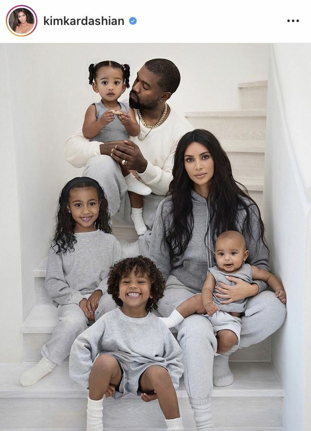 Kim Kardashian med sin make Kanye West och deras fyra barn. Kim Kardashian och Kanye West sitter i en trappa med alla sina barn och alla har grå mjukiskläder
