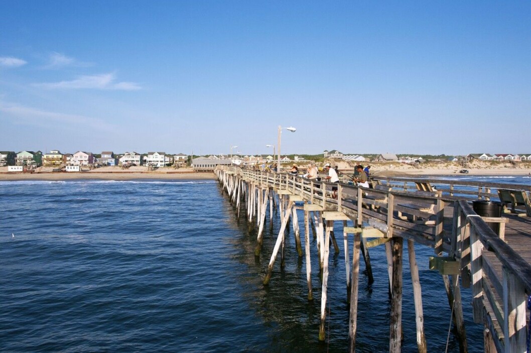 En fiskepir i Outer Banks där folk gärna samlas. En lång fiskepir i vattnet där folk står och fiskar