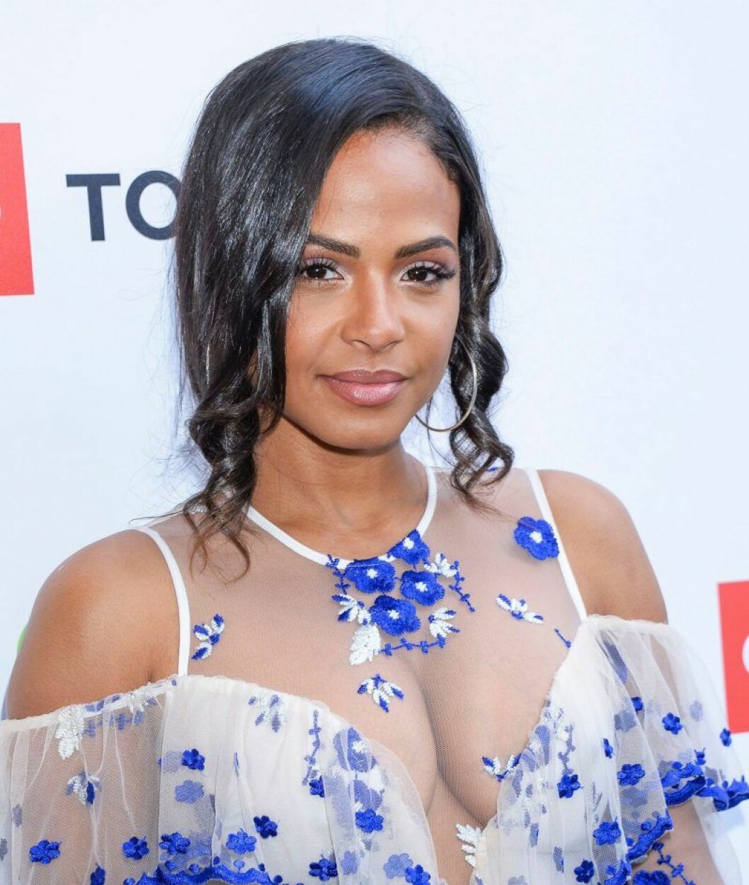 Christina Milian i lockigt hår och en vit topp med blå blommor på