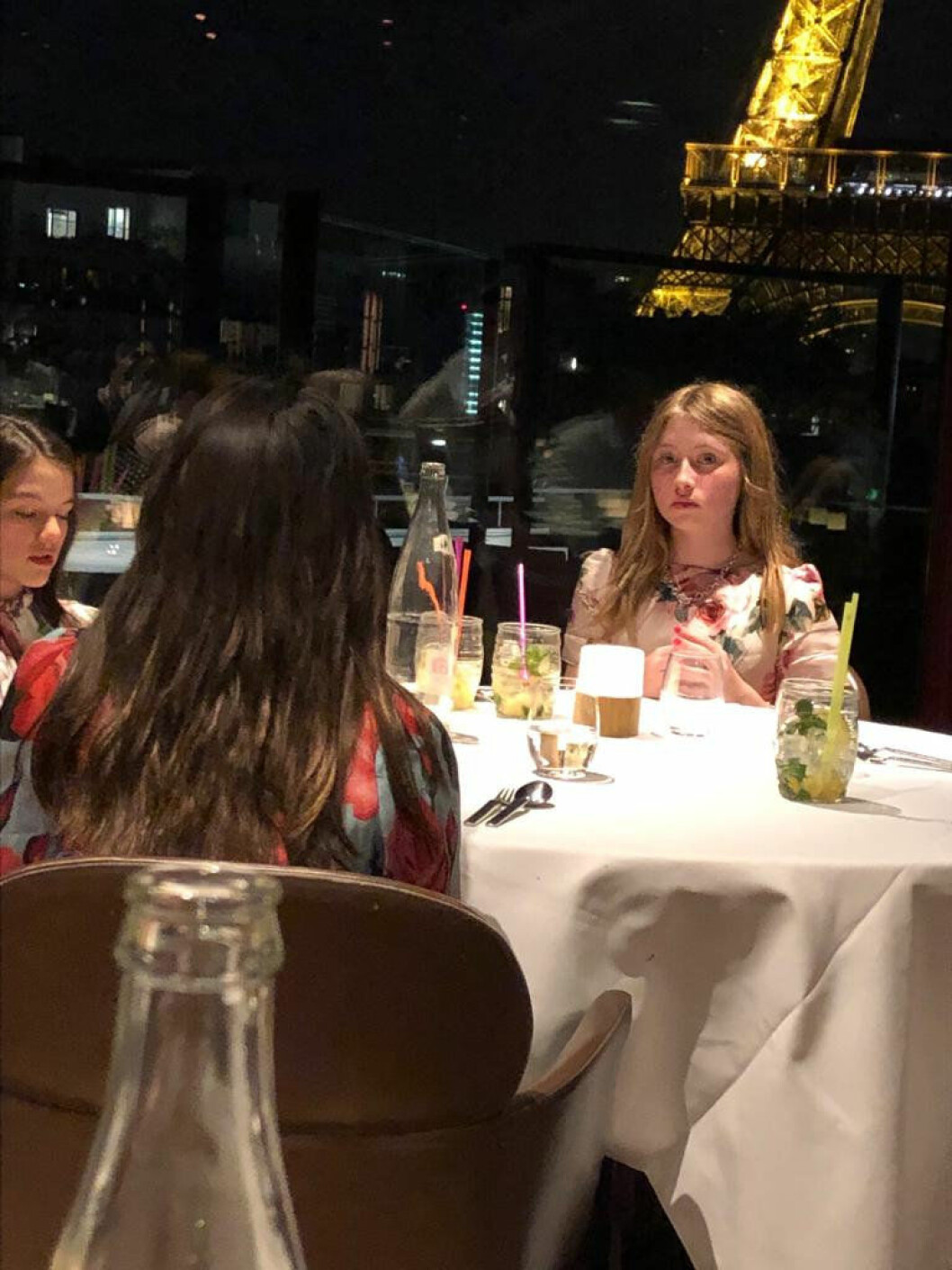 Här äter Suri Cruise och hennes vänner middag på en flott restaurang i Paris. Drinkarna är naturligtvis alkoholfria. Tre tjejer sitt rrunt ett middagsbord och väntar på maten