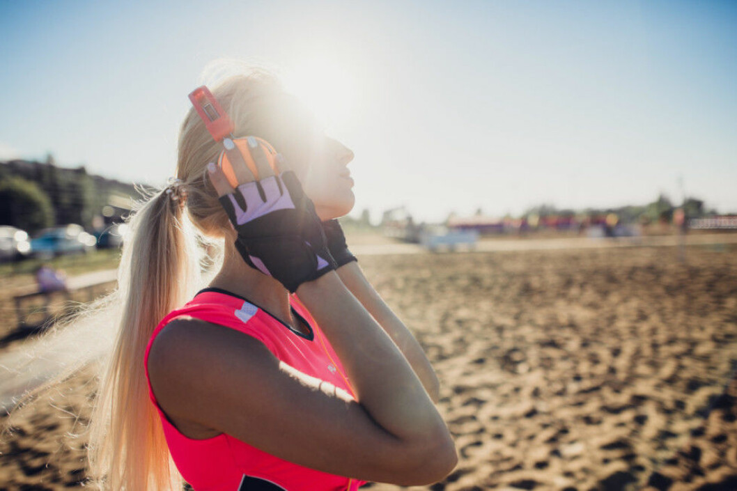 sport outdoor photo of beautiful young blonde woman in pink colorful sport suit listening to music on headphones by the beach.
